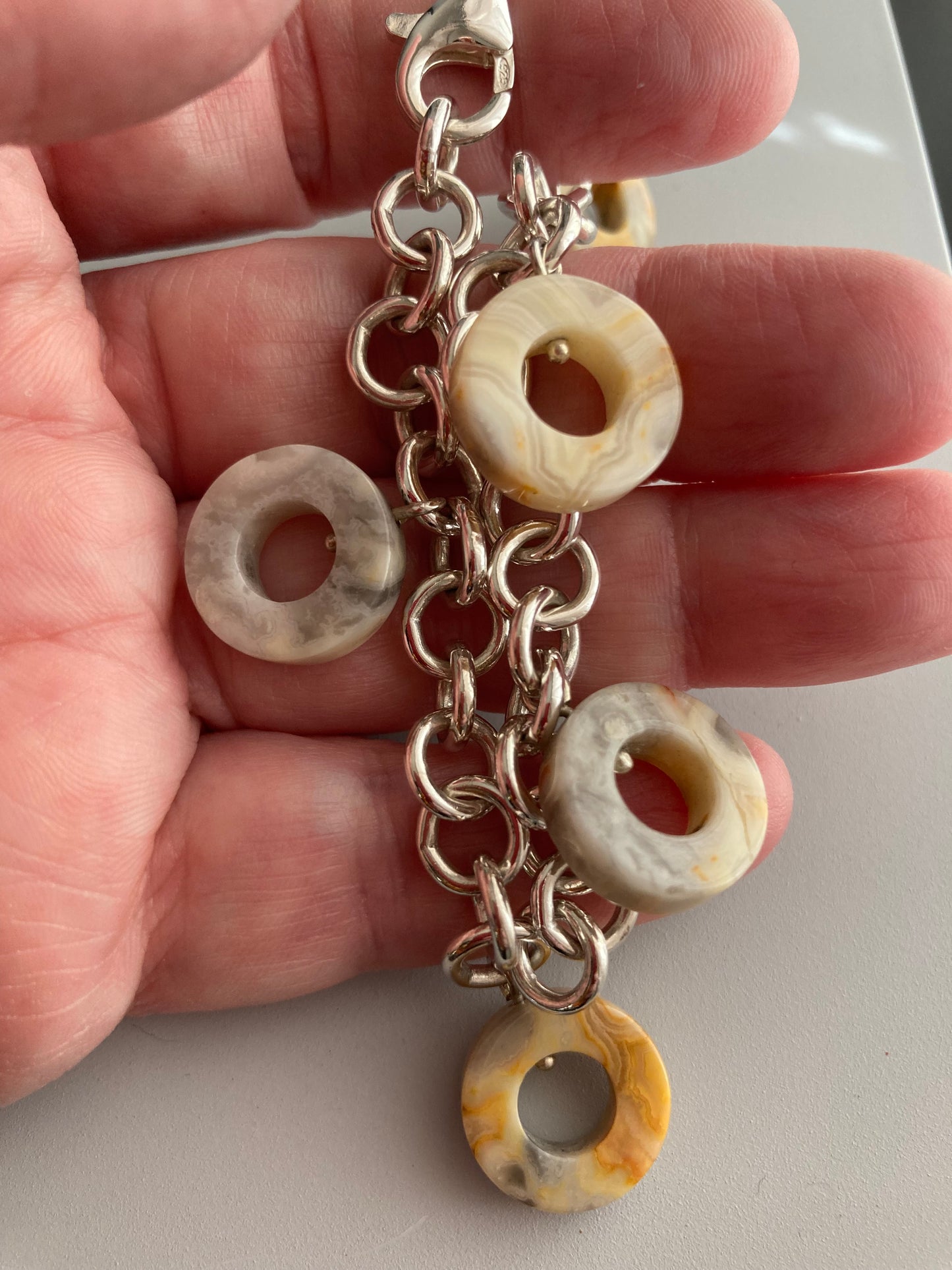 Banded agate washer shapes hanging from sterling silver chain bracelet shown on hand