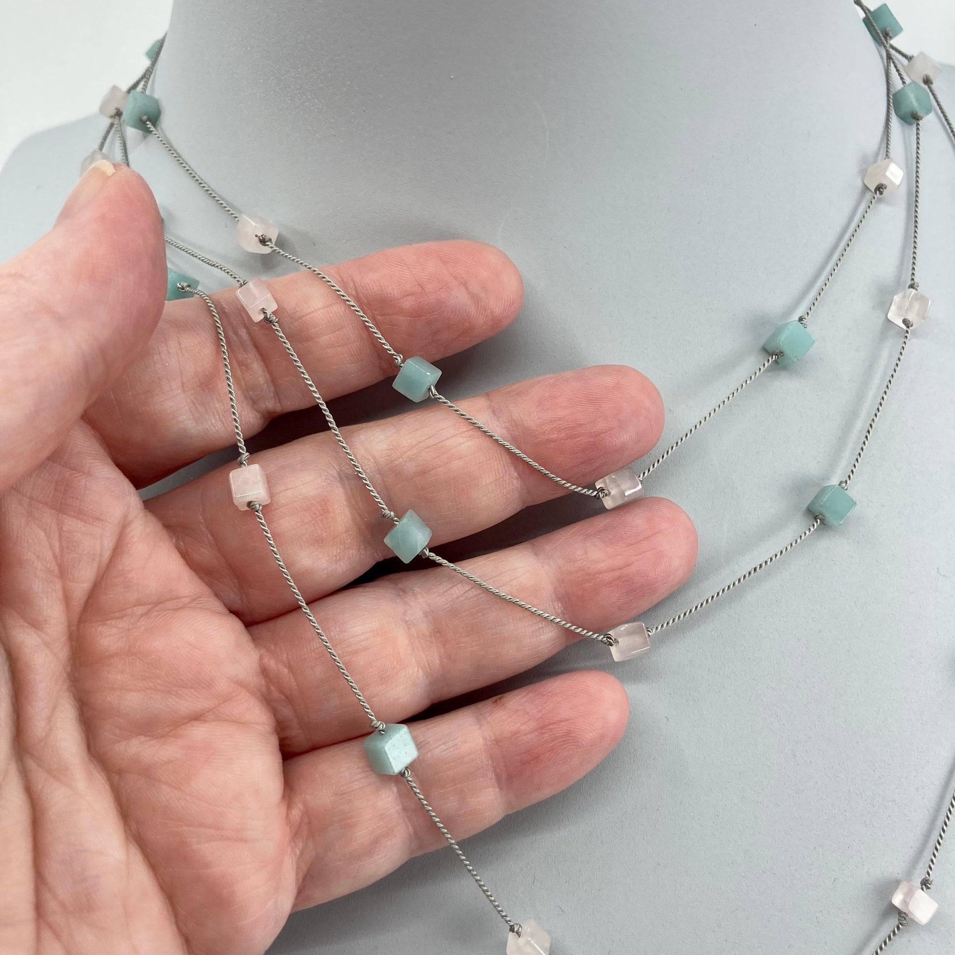 Amazonite & rose quartz cubes threaded on a silk cord tripled over bust with a section shown on hand 