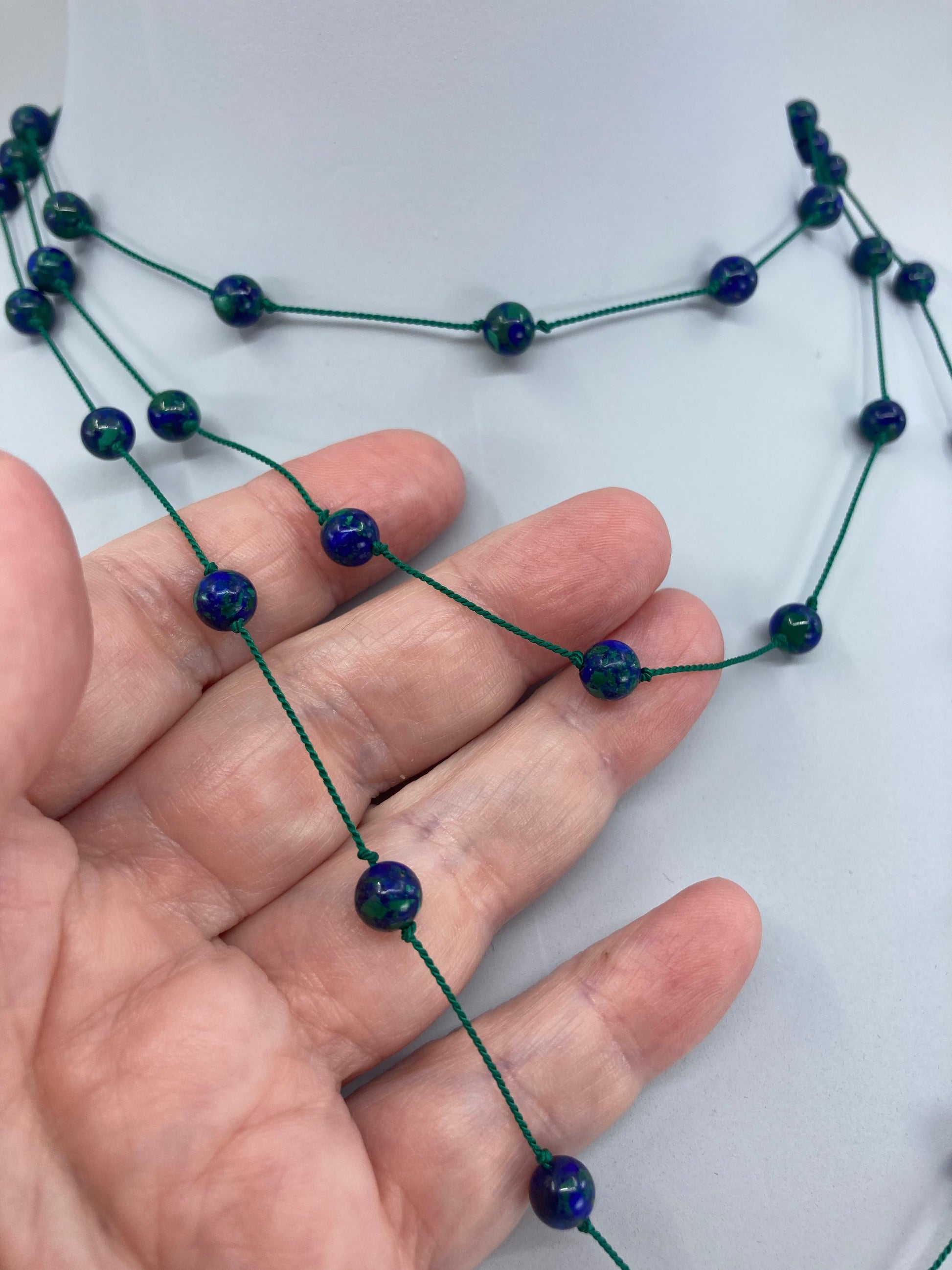 Azurmalachite beads threaded and spaced out on silk cord with sterling silver clasp necklace tripled over on display bust with hand under a section of the necklace